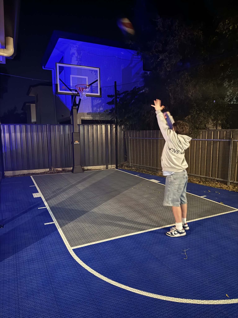 Blue tiled court lit at night with a player shooting a basketball