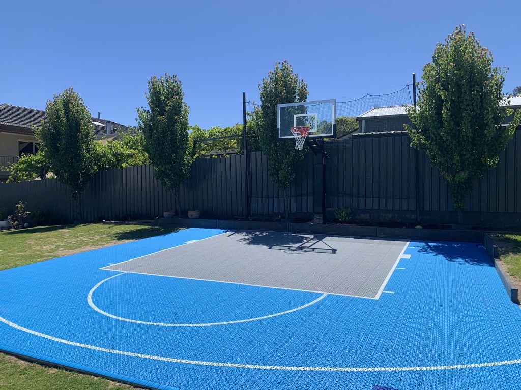 Blue and grey tiled half court with in-ground hoop and ornamental trees